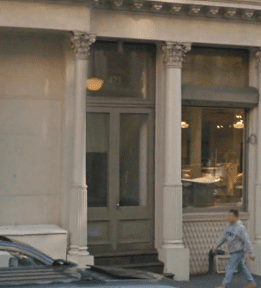 A person walking past a building with columns and glass doors.