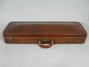 A brown leather violin case with a handle on a white surface.